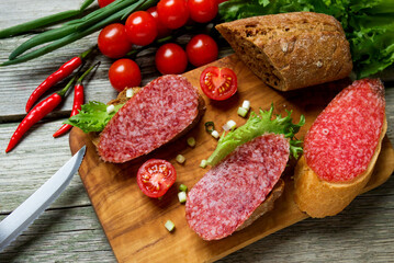 Sandwiches with dried  sausage, tomatoes, onions on a cutting board.