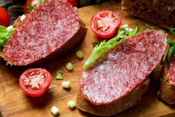 Sandwiches with dried  sausage, tomatoes, onions on a cutting board.
