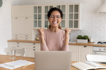 Unbelievable. Happy young latina woman sit by laptop at kitchen celebrate amazing offer invitation positive answer after job interview. Cheerful lady freelancer shout yes excited by great work result