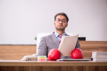 Young male employee wearing boxing gloves at workplace