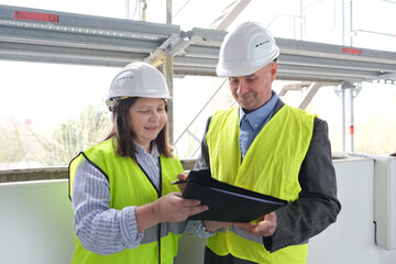 experienced elderly architect, female engineer constructor in protection of white helmet accept the object, sign documents at construction site, concept of civil engineering, cooperation