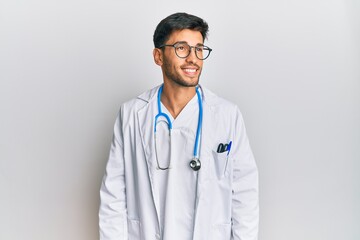 Fototapeta premium Young handsome man wearing doctor uniform and stethoscope looking away to side with smile on face, natural expression. laughing confident.
