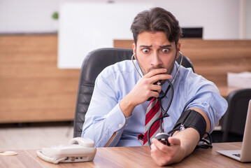 Young male employee suffering from hypertension at workplace