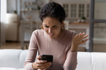 Spam mailout. Outraged nervous young latina female feel angry mad of spamming in electronic messages on smartphone. Female customer dissatisfied annoyed after reading silly email marketing letter text