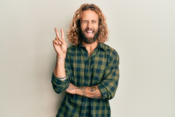 Handsome man with beard and long hair wearing casual clothes smiling with happy face winking at the...