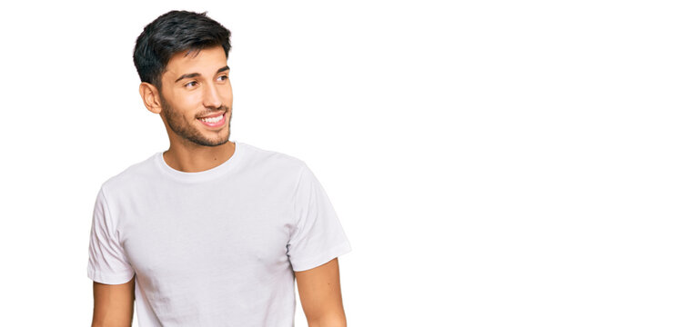 Young handsome man wearing casual white tshirt looking away to side with smile on face, natural expression. laughing confident.