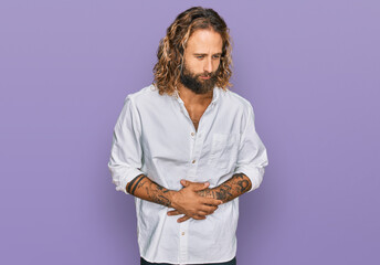 Handsome man with beard and long hair wearing casual clothes with hand on stomach because...