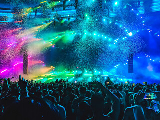 Crowd of people dancing at concert in rainbow lights