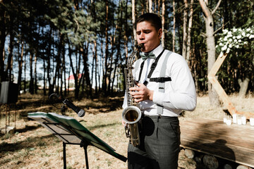 handsome young guy plays the saxophone at a gala event on the street. musical accompaniment at the...