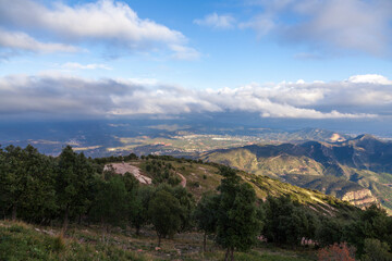 Fototapeta na wymiar Aerial view of the Montserrat mountains on a beautiful spring day, Catalonia, Spain. Dramatic sky over the mountains. Sunlight falls through the clouds on the ground and mountains.