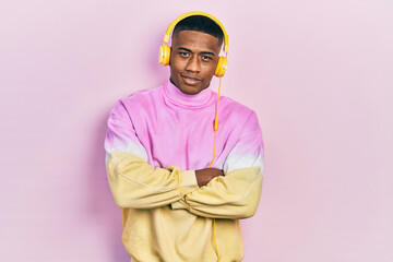 Young black man listening to music wearing headphones happy face smiling with crossed arms looking at the camera. positive person.