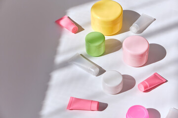 Face cream in set of multicolored jar and tubes on white table background.