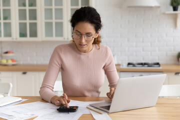 Focused millennial latin woman auditor accountant manage paperwork at home office do calculation...