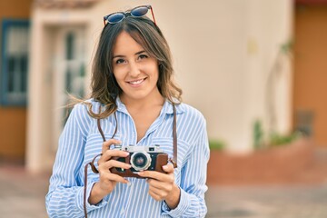 Young hispanic tourist woman smiling happy using vintage camera at the city.