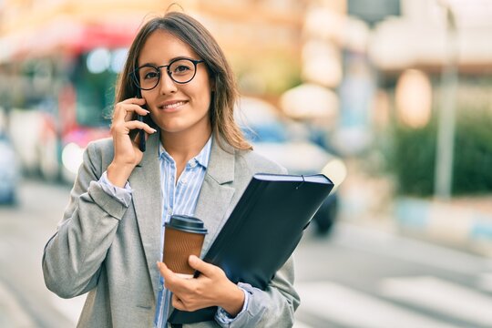 Young hispanic businesswoman talking on the smartphone and drinking take away coffee at the city.