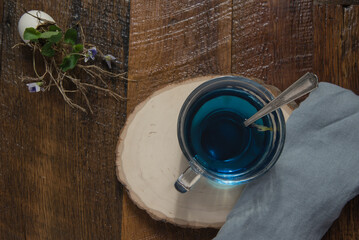 Healthy, blue, butterfly pea flower tea served on a wood slice with a blue linen napkin, small,  bouquet of violets in a repurposed eggshell on a wooden table. Top down view.
