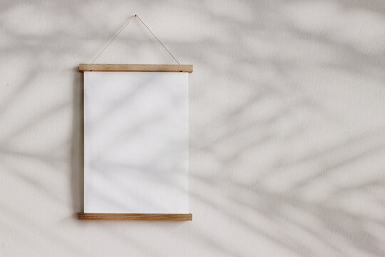 Blank wooden picture frame hanging on beige wall. Empty poster mockup for art display in sunlight. Minimal interior design.Palm leaves shadow overlay. Summer design. Copy space. No people.