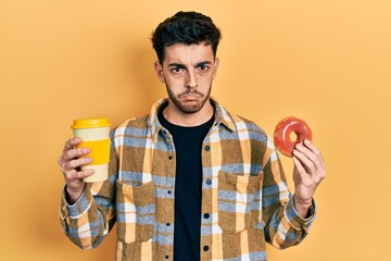 Fototapeta premium Young hispanic man eating doughnut and drinking coffee depressed and worry for distress, crying angry and afraid. sad expression.