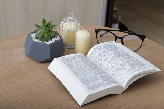 Open Holy Bible on a round table with candles, plants and glasses. Bible study at home concept