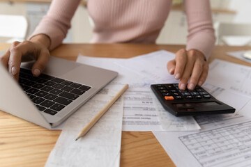 Bookkeeping requires accuracy. Young woman hands typing on computer and digital calculator keyboards preparing electronic payments of utility bills counting taxes sum balancing accounts. Close up view