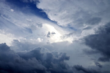 The clouds are multicolored, thunderous bizarre shapes against the blue sky and the sun above the ocean surface.