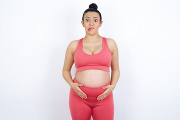 Fototapeta premium young beautiful Arab pregnant woman in sports clothes against white wall being nervous and scared biting lips looking camera with impatient expression, pensive.