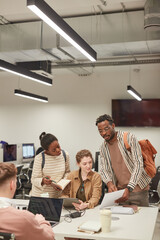 Vertical portrait of diverse group of students working together in modern school library and using...