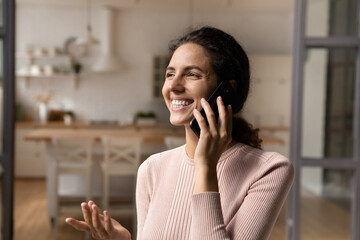 Overjoyed millennial latina female relax at home talk on phone hold telephone dialogue. Excited...