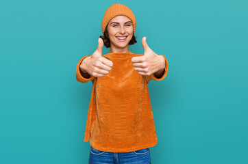 Fototapeta premium Young hispanic woman wearing casual clothes and wool cap approving doing positive gesture with hand, thumbs up smiling and happy for success. winner gesture.