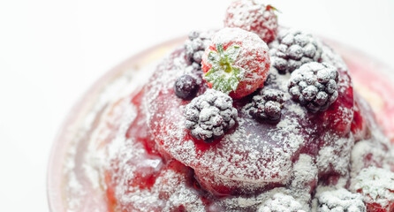 Pancakes stack with strawberries, blueberries, and blackberries, topped with sauce and sprinkled with powdered sugar