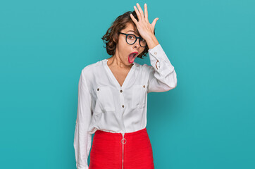 Young hispanic woman wearing business style and glasses surprised with hand on head for mistake,...