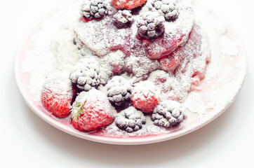 Pancakes stack with strawberries, blueberries, and blackberries, topped with sauce and sprinkled with powdered sugar
