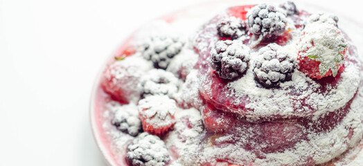 Pancakes stack with strawberries, blueberries, and blackberries, topped with sauce and sprinkled with powdered sugar