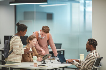 Side view at diverse group of students working together in modern school library and using computers, copy space