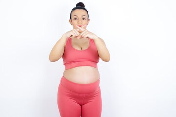 young beautiful Arab pregnant woman in sports clothes against white wall has rejection angry...