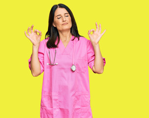 Middle age brunette woman wearing doctor uniform and stethoscope relax and smiling with eyes closed doing meditation gesture with fingers. yoga concept.