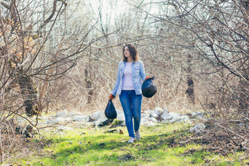 Naklejka na ściany i meble Young beautiful female volunteer collects plastic garbage in the forest and park, volunteer holding a bag with collected plastic and garbage