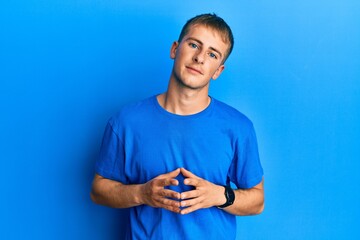 Young caucasian man wearing casual blue t shirt hands together and fingers crossed smiling relaxed and cheerful. success and optimistic