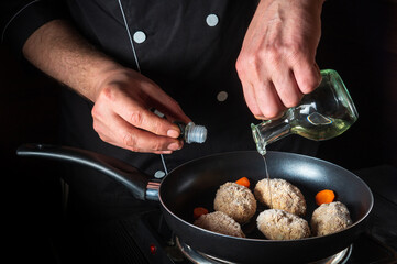 Cooking beef cutlets in a grill pan with the hands of a chef on a black background for copying the space text restaurant menu. Chef or cook adds oil