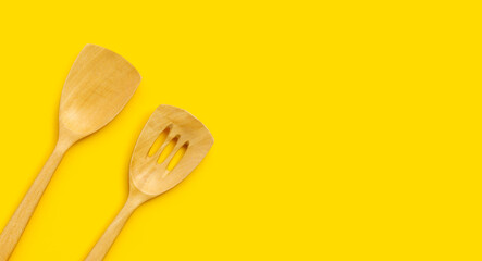 Wooden kitchen spatula on yellow background.