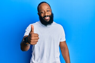 Young african american man wearing casual white tshirt doing happy thumbs up gesture with hand. approving expression looking at the camera showing success.
