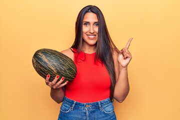 Young beautiful brunette woman holding melon smiling happy pointing with hand and finger to the side