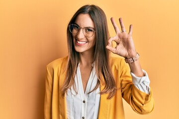 Young beautiful woman wearing business style and glasses smiling positive doing ok sign with hand and fingers. successful expression.