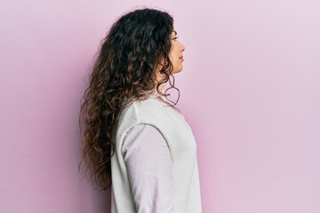 Young brunette woman with curly hair wearing casual clothes looking to side, relax profile pose with natural face and confident smile.