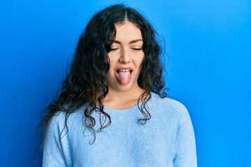 Young brunette woman with curly hair wearing casual clothes sticking tongue out happy with funny...