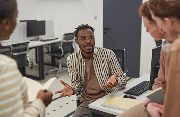 Portrait of African-American man talking to colleagues in office and gesturing actively while collaborating on project