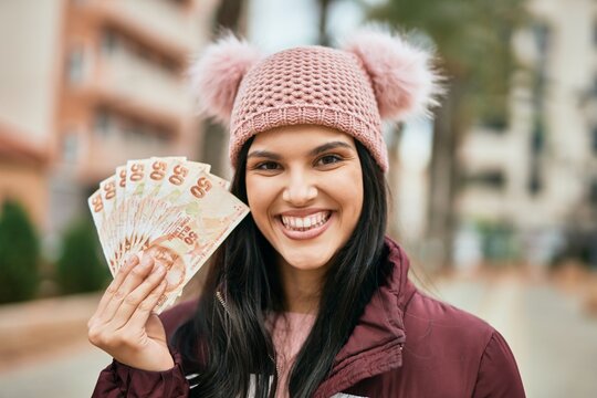 Young hispanic girl smiling happy holding turkish lira banknotes at the city.