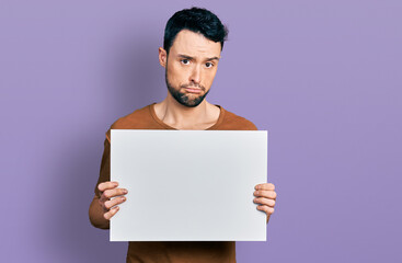 Hispanic man with beard holding blank empty banner depressed and worry for distress, crying angry...