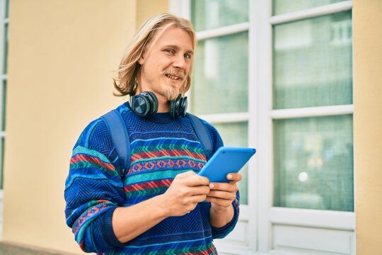 Young scandinavian student man using headphones and touchpad at the city.