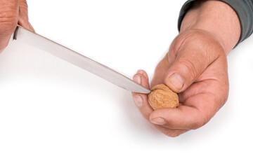 Hands of an elderly man with a knife cracking a walnut in his hand on a white background, isolated